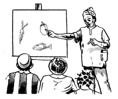 Un agent de santé communautaire qui enseigne la nutrition aux hommes et aux femmes. Il montre du doigt un tableau avec des dessins d’aliments sains : fruits, légumes et poissons.