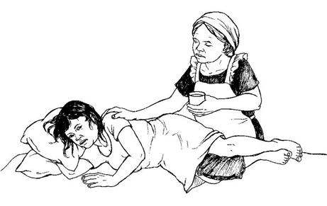 Une personne qui s’occupe d’une personne très malade. La personne malade est allongée confortablement avec des coussins. Le soignant offre un verre et pose une main sur l’épaule du malade.